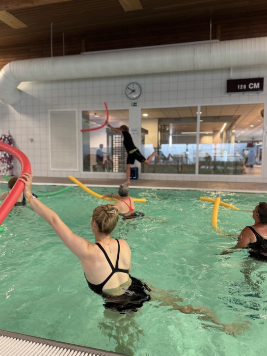 Mensen doen aquagym in een zwembad met kleurrijke drijvende buizen. (vergroot foto)