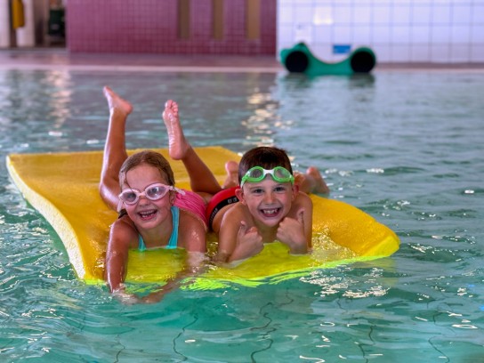 Twee lachende kinderen liggen op een geel vlot in het zwembad. (vergroot foto)